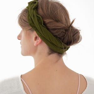 K&ouml;nnte beinhalten: Olivgr&uuml;nes Stirnband aus weichem Stoff. Das Stirnband ist um den Kopf gewickelt und oben gebunden. Die Person tr&auml;gt ein wei&szlig;es Oberteil mit einem rosa Tr&auml;ger. Haare sind zu einem Dutt frisiert.