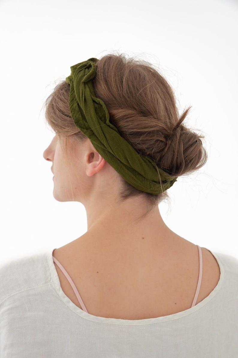 K&ouml;nnte beinhalten: Olivgr&uuml;nes Stirnband aus weichem Stoff. Das Stirnband ist um den Kopf gewickelt und oben gebunden. Die Person tr&auml;gt ein wei&szlig;es Oberteil mit einem rosa Tr&auml;ger. Haare sind zu einem Dutt frisiert.