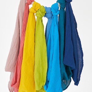 K&ouml;nnte beinhalten: Eine Sammlung von geknoteten Schals in Regenbogenfarben, von Rosa bis Marineblau. Die Schals aus strukturiertem Stoff h&auml;ngen an einem wei&szlig;en Seil. Die Farben umfassen Rosa, Rot, Gelb, Gr&uuml;n und verschiedene Blaut&ouml;ne.