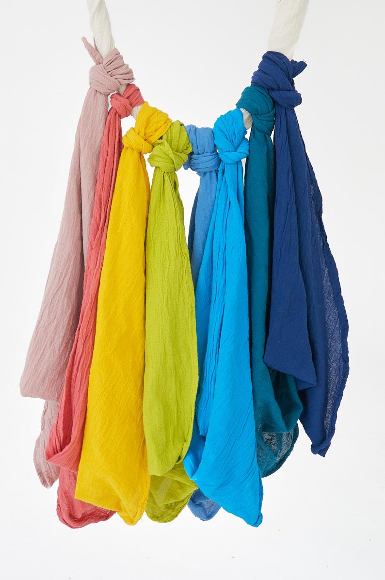 K&ouml;nnte beinhalten: Eine Sammlung von geknoteten Schals in Regenbogenfarben, von Rosa bis Marineblau. Die Schals aus strukturiertem Stoff h&auml;ngen an einem wei&szlig;en Seil. Die Farben umfassen Rosa, Rot, Gelb, Gr&uuml;n und verschiedene Blaut&ouml;ne.