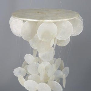 Pode incluir: Um móbile suspenso com um disco superior circular do qual pendem numerosos discos de concha circulares, translúcidos e de cor esbranquiçada, através de fios finos e transparentes. Os discos estão dispostos em vários níveis em cascata.
