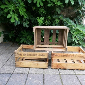 Könnte beinhalten: Zwei Holzkisten mit dem Aufdruck "Wein aus deutschen Landen" und "Wein schenkt Freude". Die Kisten sind übereinander gestapelt.