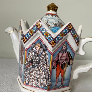 Pode incluir: Uma chaleira de cerâmica branca com um design em forma de coroa. A chaleira apresenta ilustrações de figuras históricas e um botão dourado. As bordas são aparadas com ouro, e o design inclui padrões florais e geométricos.