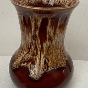 May include: A brown ceramic vase with a glossy finish. The vase has a wide, flared rim and a rounded body. The exterior features a textured, dripped design in shades of brown and cream, creating a unique, organic aesthetic.