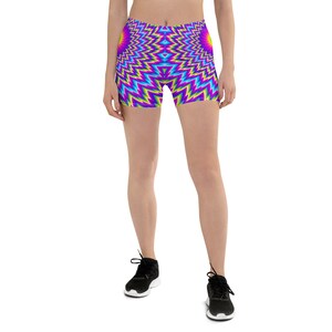 May include: Vibrant, eye-catching shorts featuring a repeating zigzag pattern in shades of purple, blue, yellow, and green. The shorts are worn with black athletic shoes. The design creates an optical illusion.