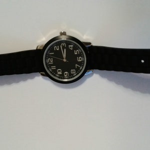 May include: A black wristwatch with a black rubber band and a black face with white numbers. The watch has silver hands.
