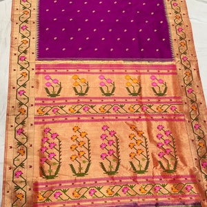 Pode incluir: Um sari roxo vibrante com uma borda dourada e um design floral. O sari apresenta um padrão detalhado de flores rosa e amarelas em um fundo dourado. A borda tem um design geométrico com detalhes verdes e dourados.