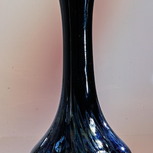 May include: A tall, elegant vase with a flared top and a bulbous base. The vase is a deep, glossy black with iridescent blue and green accents. The base has a textured, patterned design. A decorative home accent.