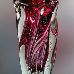 Pode incluir: Um vaso de vidro cilíndrico e alto com um esquema de cores magenta profundo e transparente. O design incorpora padrões orgânicos em espiral com numerosas pequenas bolhas de ar suspensas por toda a estrutura de vidro espesso.