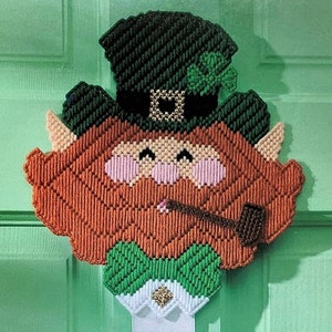 May include: A green, white, and orange crocheted leprechaun with a pipe and a shamrock on his hat.