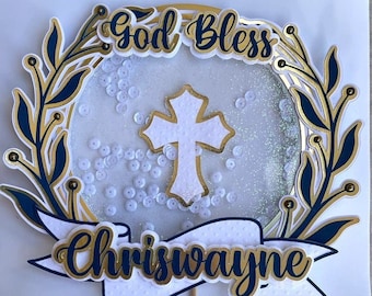 May include: A white cake topper with a gold cross, a blue and gold banner with the text "God Bless Chriswayne", and a wreath of gold and blue leaves.