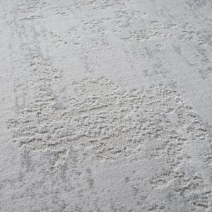 May include: Close-up of a light gray rug with a textured, abstract design. The pattern features raised, irregular shapes in a lighter shade of gray, creating a subtle, layered effect. The rug's surface appears soft and plush, suitable for home decor.