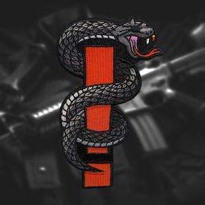 May include: A black and gray embroidered patch of a snake wrapped around a red and black vertical bar. The snake has a white tongue and a menacing expression.