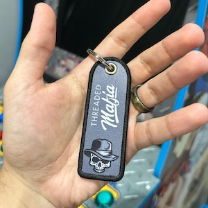May include: A gray key chain with the text "THREADED Mafia" and a skull wearing a fedora hat.