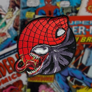 May include: A red and black embroidered patch featuring a yin yang symbol with Spider-Man on one side and Venom on the other.