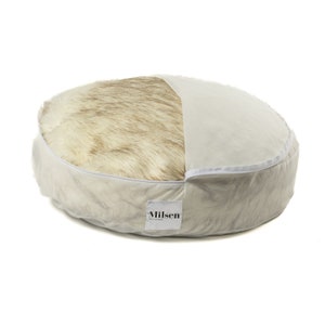 May include: A round, cream-colored dog bed with a removable faux fur insert. The bed has a white label with the word "Milsen" printed on it.