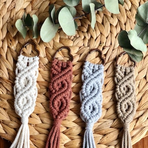 May include: Four handmade macrame keychains with heart-shaped metal rings. The keychains are in white, rust, grey, and beige.