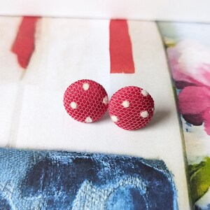 May include: A pair of red and white polka dot fabric earrings. The earrings are round and have a white mesh fabric with red polka dots.