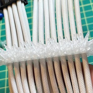May include: A close-up of a white cable management system with a clear plastic cable organizer. The organizer has a spiky design and is used to keep the cables neat and organized.