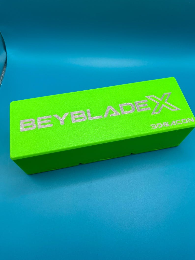 May include: A vivid green rectangular box featuring the silver text "BEYBLADE X" and "3DEACON". The box is presented against a blue backdrop, creating a striking contrast.