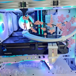 May include: A custom white computer case with internal components lit by LEDs. The case features pink cherry blossom decorations and crystal-shaped accents. A Radeon graphics card is visible.