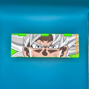 May include: A rectangular box with green edges, displaying a detailed illustration of a character with white hair and intense eyes. The character's face is centered, with the text "GAME MAN" on the right.