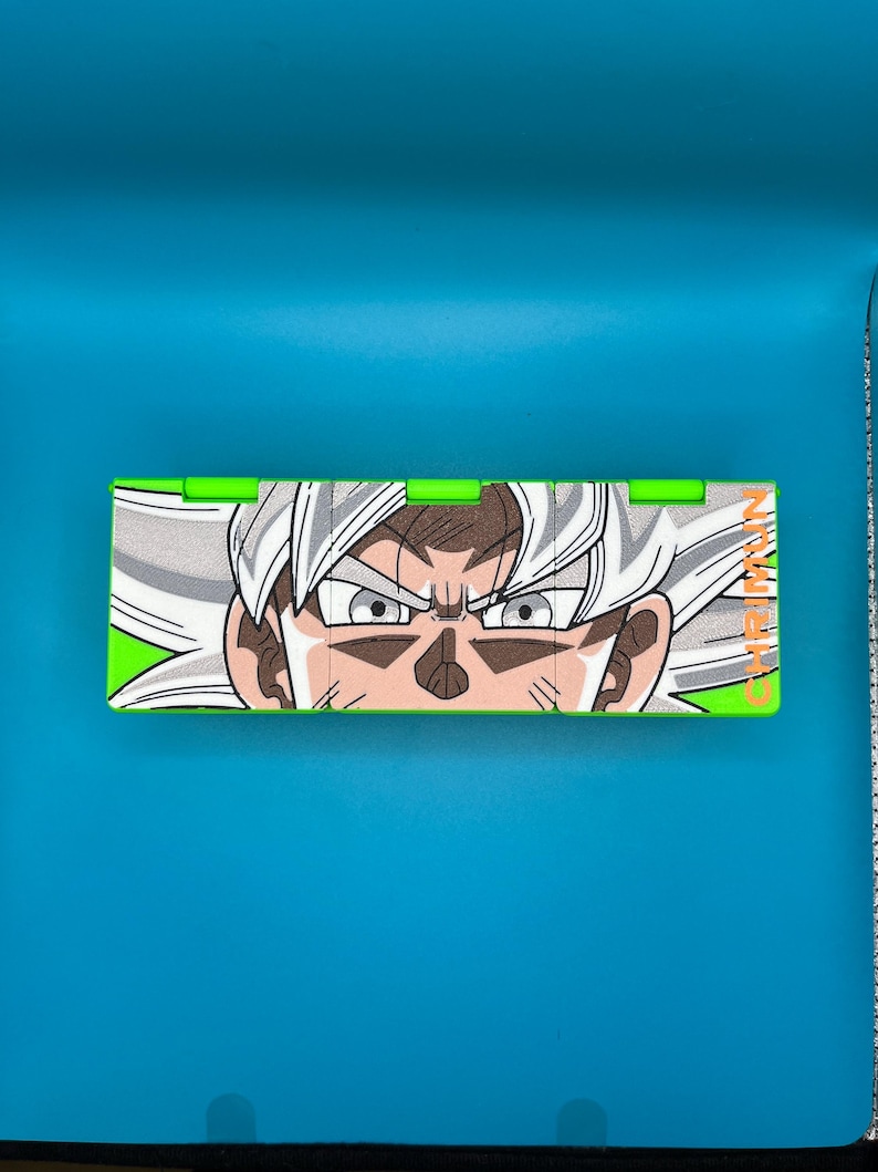 May include: A rectangular box with green edges, displaying a detailed illustration of a character with white hair and intense eyes. The character's face is centered, with the text "GAME MAN" on the right.