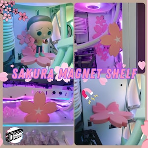 Op de afbeelding: Een witte computerbehuizing met roze en witte magnetische planken in de vorm van kersenbloesems. De planken zijn aan de zijkant van de behuizing bevestigd en houden een klein beeldje vast. De tekst "SAKURA MAGNET SHELF" is zichtbaar op de behuizing. De tekst "MAGNETIC MOD" is zichtbaar aan de linkerkant van de afbeelding. De tekst "SAKURA STORM SET" is zichtbaar aan de rechterkant van de afbeelding.