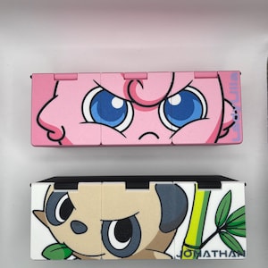 May include: Two colorful, hinged boxes. The top box is pink with a cartoon face and blue eyes. The bottom box is white and tan with a cartoon face, green bamboo, and the name "JONATHAN".