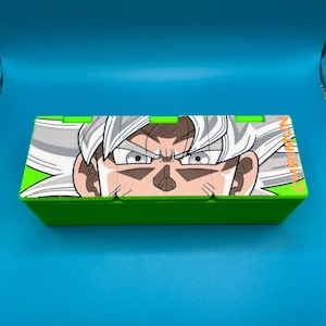 May include: A green box with a detailed illustration of a character's face with white hair and intense eyes. The box has a bright green border and a blue background.