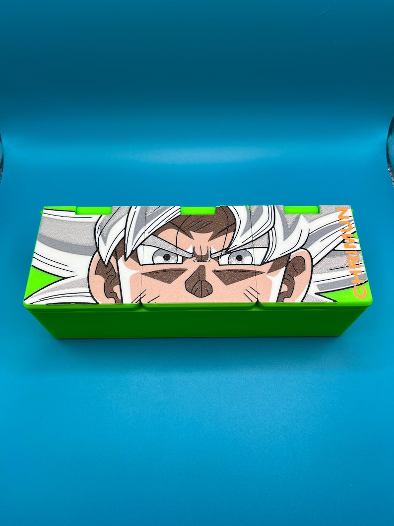May include: A green box with a detailed illustration of a character's face with white hair and intense eyes. The box has a bright green border and a blue background.