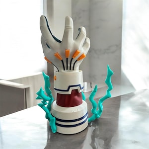 Puede incluir: Una escultura de mano rob&oacute;tica blanca con detalles naranjas similares a cables en el dorso, una base cil&iacute;ndrica de color rojo oscuro y blanco con rayas azules horizontales, y dos efectos de energ&iacute;a en forma de rayos de color turquesa brillante.
