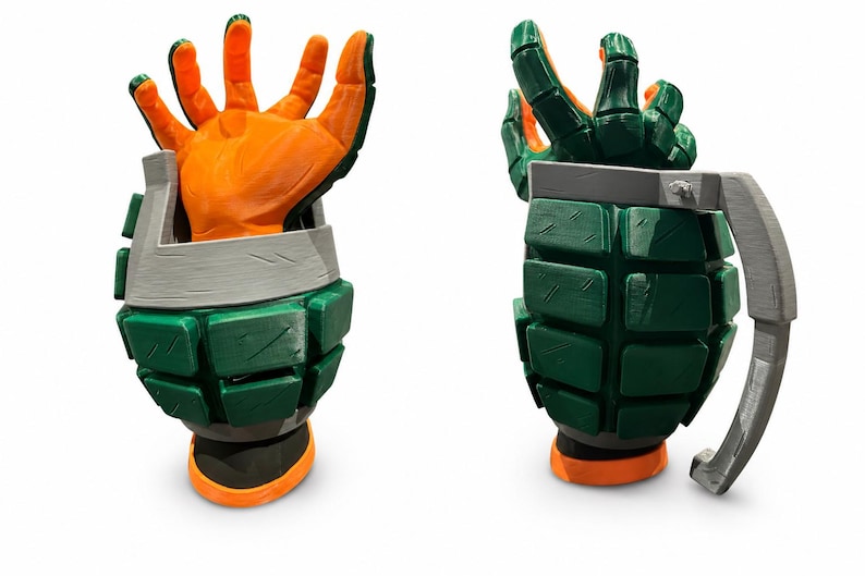 Puede incluir: Una taza impresa en 3D con forma de granada, cuerpo texturizado verde, asa gris y una mano naranja que emerge de la parte superior. El dise&ntilde;o presenta un exterior segmentado con l&iacute;neas de capa visibles y una base plana, en dos &aacute;ngulos.