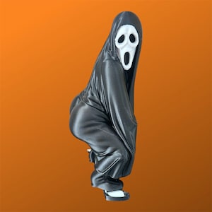 May include: A small figurine of a character wearing a black hooded robe and a white mask with a wide, open-mouthed expression. The figure is posed in a crouching position, showing a black draped garment and visible white footwear at the base.