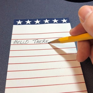 May include: A white notepad with red stripes and blue stars at the top. The notepad has lined paper and the words "HELLO THERE" are written on the first line.