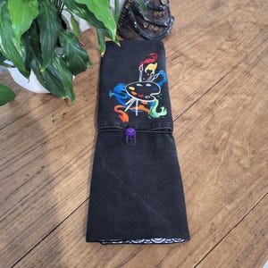 Peut inclure: Étui enroulable en toile noire avec une palette de peinture colorée et des pinceaux brodés sur le devant. L'étui est doté d'une fermeture à pression violette.