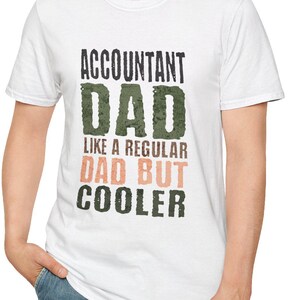 以下が含まれることがあります： 「ACCOUNTANT DAD LIKE A REGULAR DAD BUT COOLER」のテキストが黒、緑、ピーチ色でプリントされた白いTシャツ。クルーネックのシャツが着用されています。