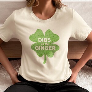 Może przedstawiać: Biała koszulka z zielonym nadrukiem koniczyny czteroliściennej z napisem "DIBS on the GINGER".