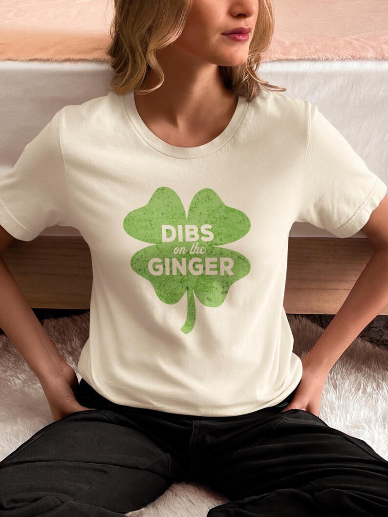 Może przedstawiać: Biała koszulka z zielonym nadrukiem koniczyny czteroliściennej z napisem "DIBS on the GINGER".