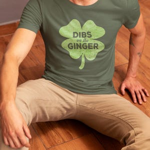 Może przedstawiać: Zielona koszulka z grafiką koniczyny czteroliściennej i tekstem "DIBS on the GINGER" w kolorze czarnym.