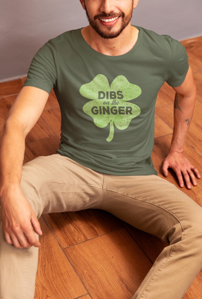 Może przedstawiać: Zielona koszulka z grafiką koniczyny czteroliściennej i tekstem "DIBS on the GINGER" w kolorze czarnym.