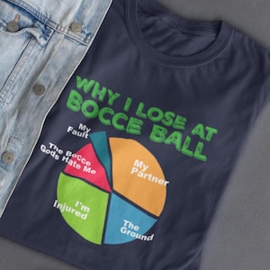 May include: Navy blue t-shirt with the text "WHY I LOSE AT BOCCE BALL" in green. A pie chart graphic lists reasons for losing, including "My Fault," "My Partner," "The Ground," "I'm Injured," and "The Bocce Gods Hate Me."