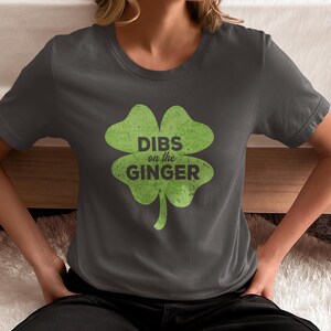 Może przedstawiać: Szary t-shirt z zielonym nadrukiem koniczyny czteroliściennej. Koniczyna zawiera napis "DIBS on the GINGER" wewnątrz.