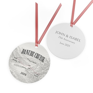 May include: Two round, white ornaments with red ribbon. One features a Danube Cruise map with text "DANUBE CRUISE" and "2025". The other ornament has the text "JOHN & ISABEL 25th Anniversary June 2025".