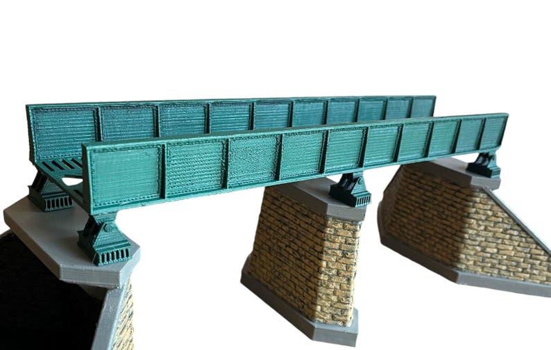 May include: A model train bridge made of green metal with brick supports. The bridge is designed for use with model train sets.