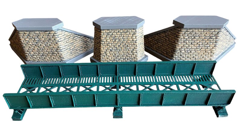 May include: Three brick abutments with a green metal bridge in between. The bridge has a lattice design and is made of metal.