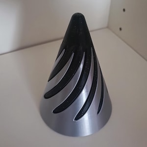 Op de afbeelding: Een zwart en zilveren kegelvormig object met een decoratief patroon. Het object is gemaakt van een glad, glanzend materiaal.