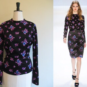 May include: A black long-sleeved shirt with a floral print featuring purple and blue flowers on a black background.