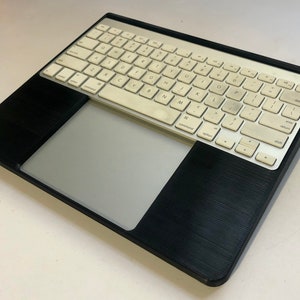 May include: A black laptop stand with a white keyboard and a gray trackpad. The stand has a textured surface.