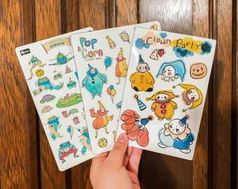 May include: Three colorful sticker sheets featuring illustrations of clowns, frogs, and popcorn. The sheets are titled "Food Circus", "Pop Corn Clown Food", and "Clown Party".
